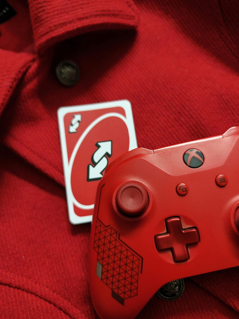 A red Xbox controller with a reverse Uno card on a red fabric background, perfect for gaming themes.