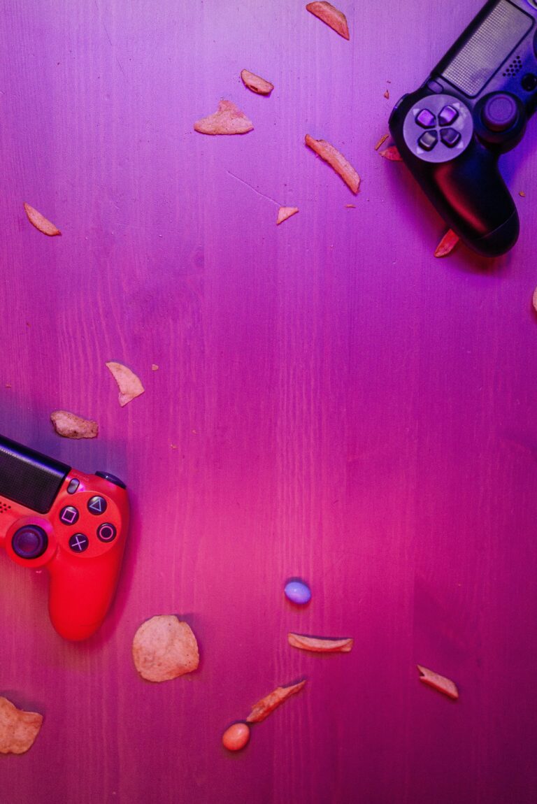 Top view of gaming controllers on a vibrant surface scattered with snacks.